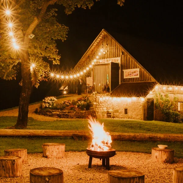 Svētku šķūnis vakara gaismā ar gaismiņu virtenēm un ugunskuru